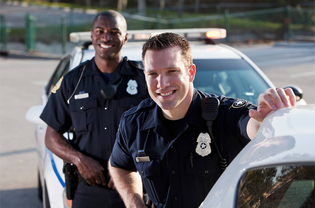 Two police officers standing and smiling in front of their patrol car